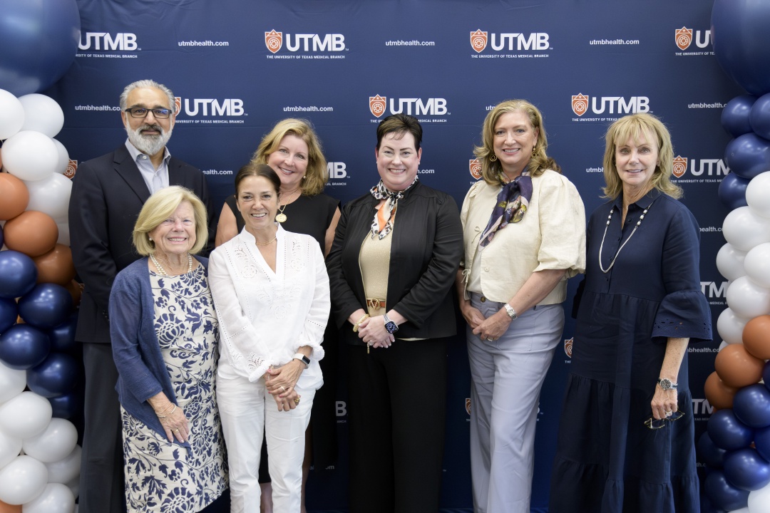 Seven people stand in two rows in front of a UTMBâ€‘branded backdrop, flanked by balloon columns in navy, white, and orange. Dr. Gulshan Sharma, far left, is pictured with Kristen Starnes-Ott, PhD, center, and members of the UTMB School of Nursing Advisory Council.